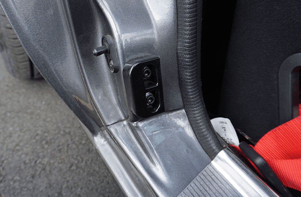 Close-up of a car door frame showing a black control panel with two adjustment buttons, possibly for wing mirror control, beside a red seat belt.