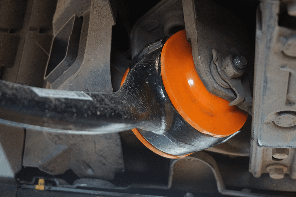 Close-up of an orange shock absorber in the suspension system of a vehicle, showing detailed elements like dust on the components and surrounding metallic parts.