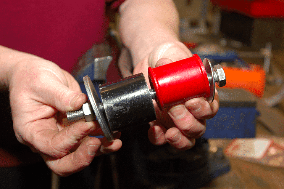 Close-up of hands holding a freshly assembled cylindrical device with red and black components and metallic bolts, in a workshop environment.
